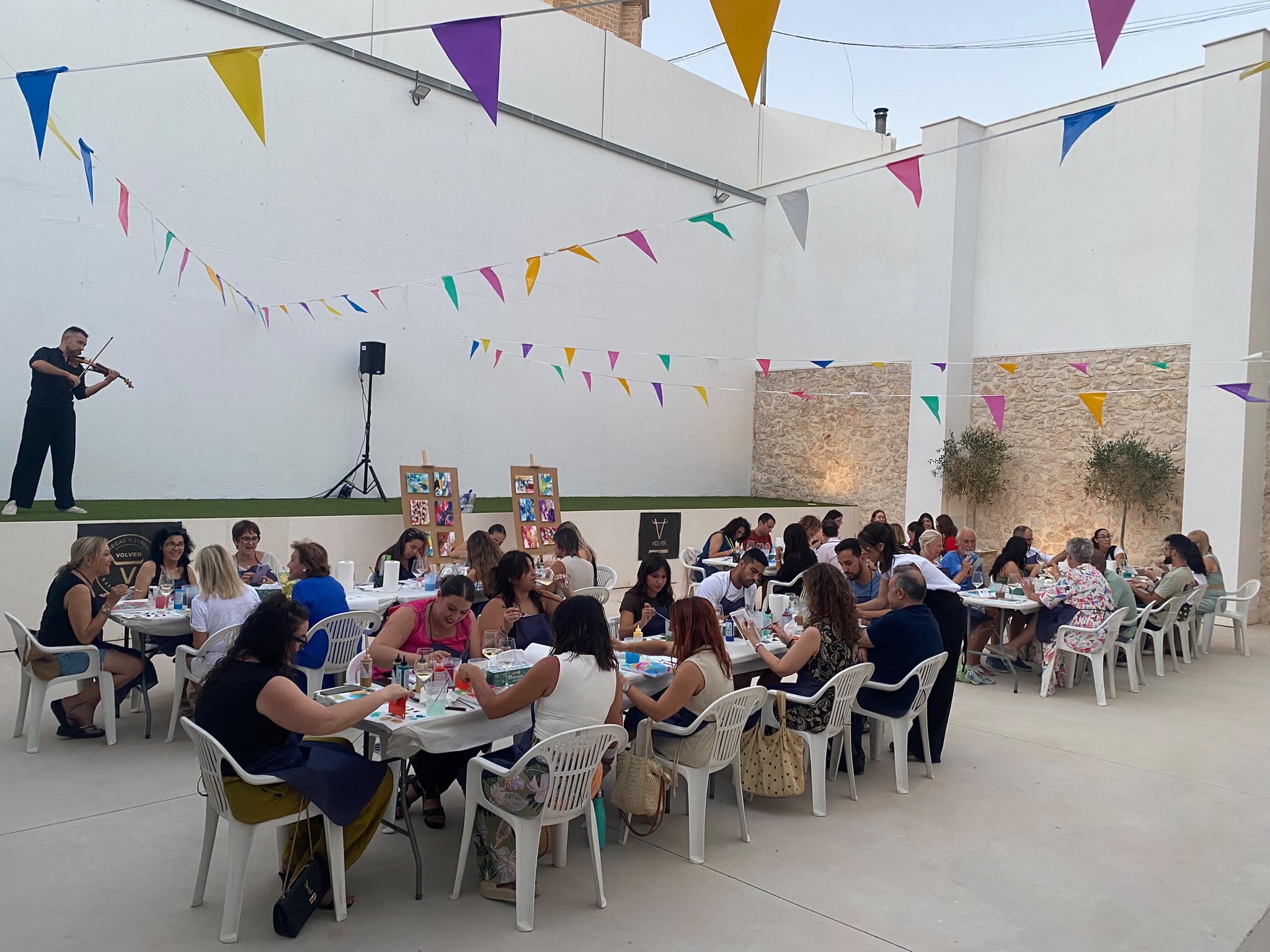 Vista general del taller Arte y Vino en el patio de la Casa de Don Pedro, con participantes pintando y música de violín en directo