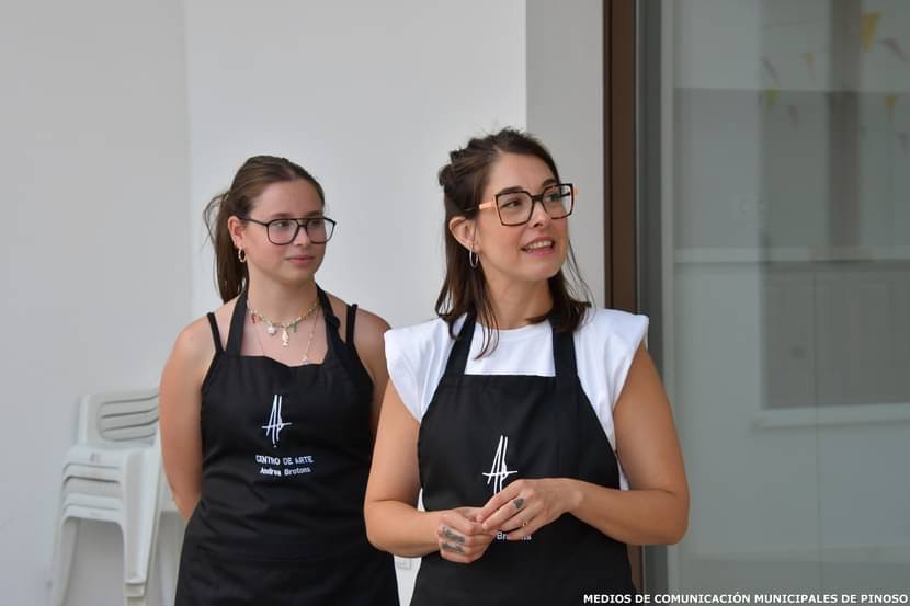 Andrea Brotons y una colaboradora presentan el taller con los delantales del Centro de Arte Andrea Brotons