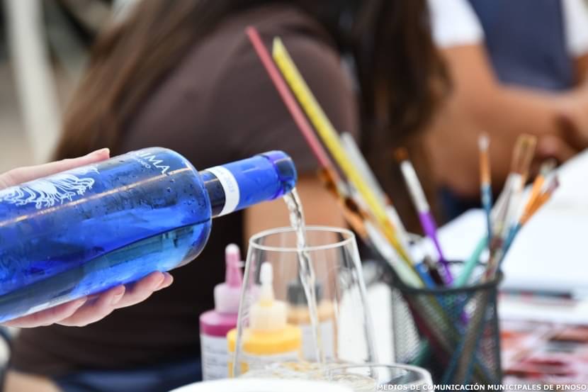 Detalle de una botella sirviendo vino junto a pinceles y materiales artísticos